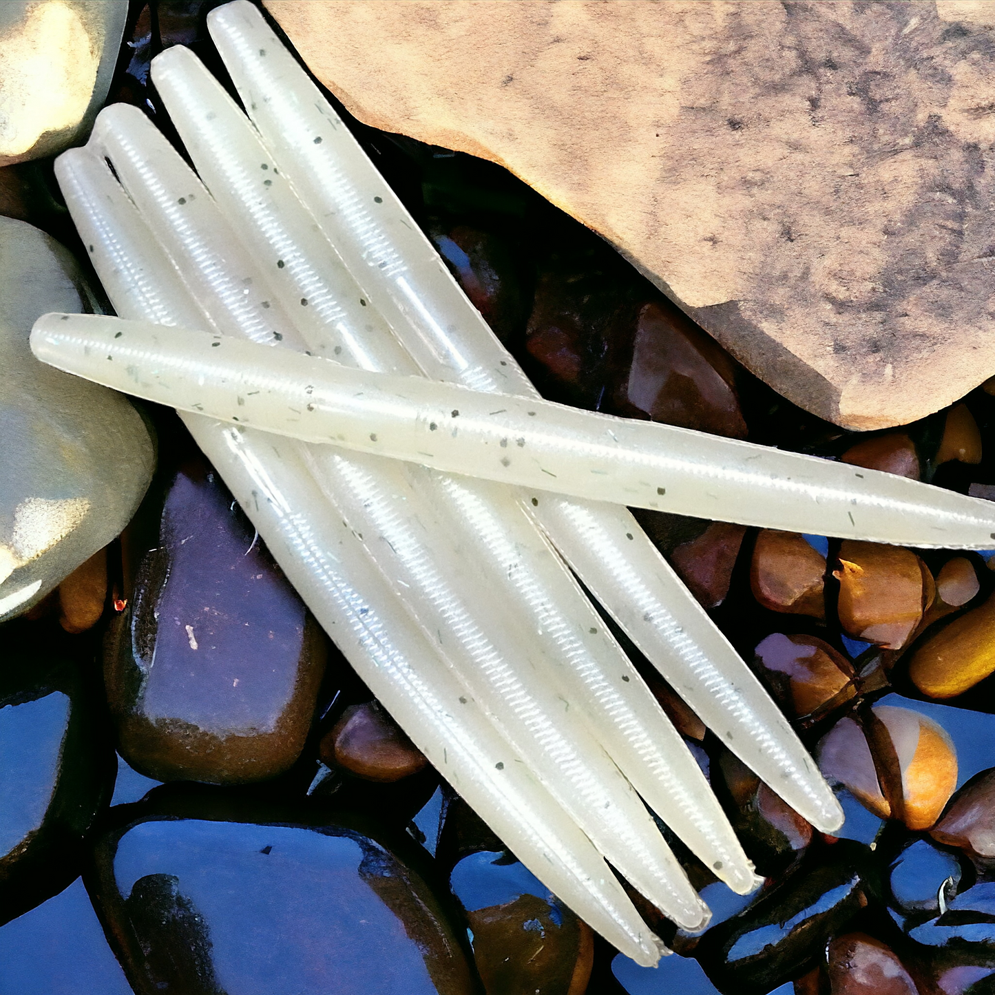 Nasties Stick Worms, 5-inch translucent white soft plastics with black specks, 10-pack on river rocks.